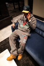 Person wearing a gray hoodie and pants with Noble Mansion logos, sitting on a blue couch.